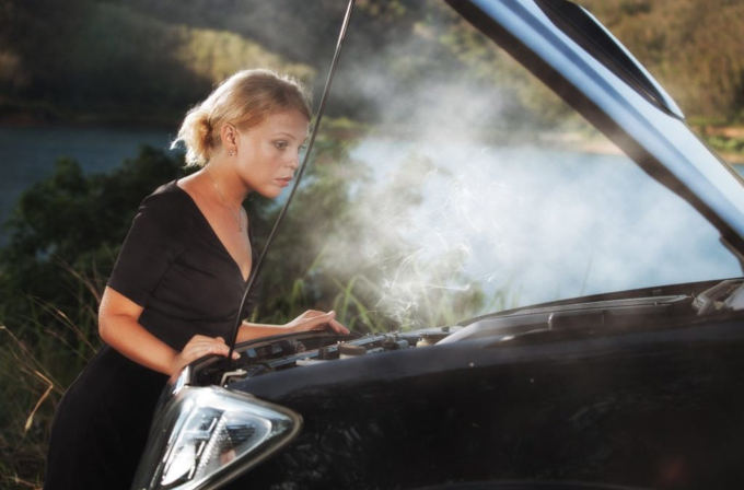 woman looking worried under smoking hood of car