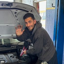 Ron Harrop III, Automotive Technician of AAMCO in South Tampa, working under the hood of a car in the shops garage, waving hello