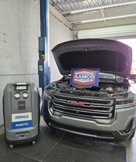 AAMCO technician servicing GMC vehicle with AC recovery machine for car air conditioning maintenance